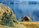 In Vordergrund ist ein Kunstwerk aus Kupfer. In Hintergrund sieht man den eisblauen Fjord und eine kleine mit grnen Gras bedeckten Htte
